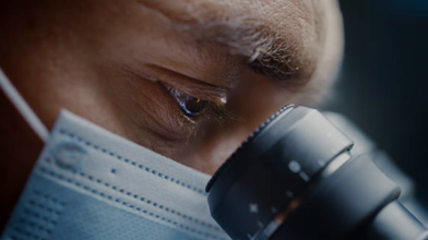Scientist wearing surgical mask and looking into microscope.png